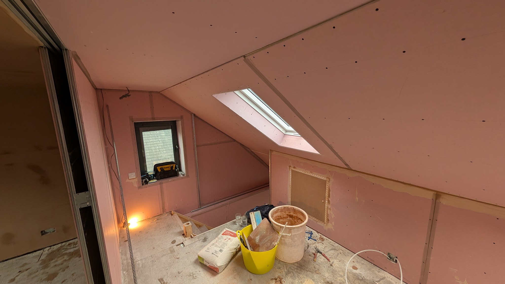 Loft room under the eaves boarded in pink plasterboard with a roof window