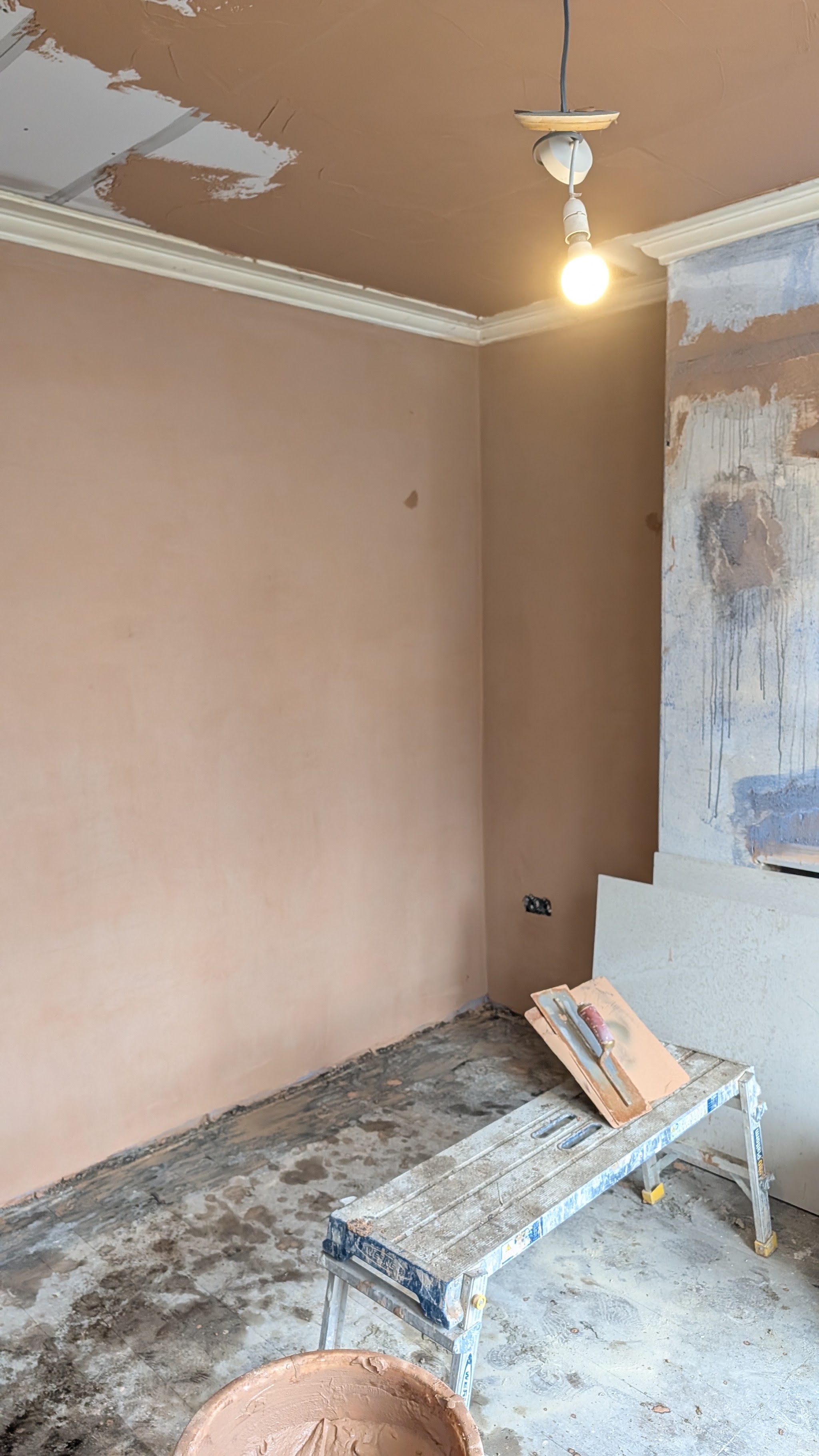 Freshly plastered walls and ceiling still drying to a pink finish, with a work platform in the room