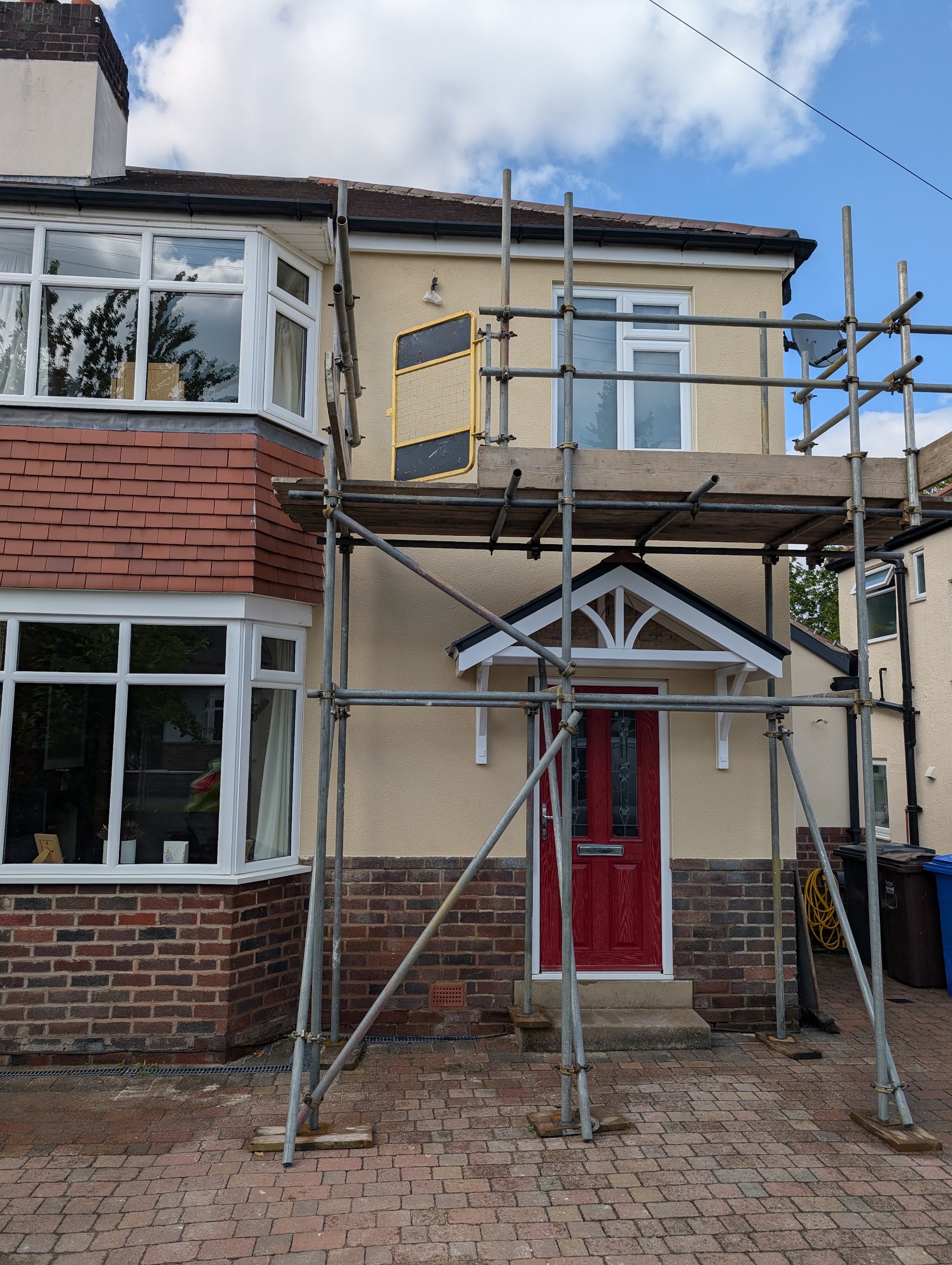 1930s semi-detached house under scaffolding with a freshly rendered cream upper storey