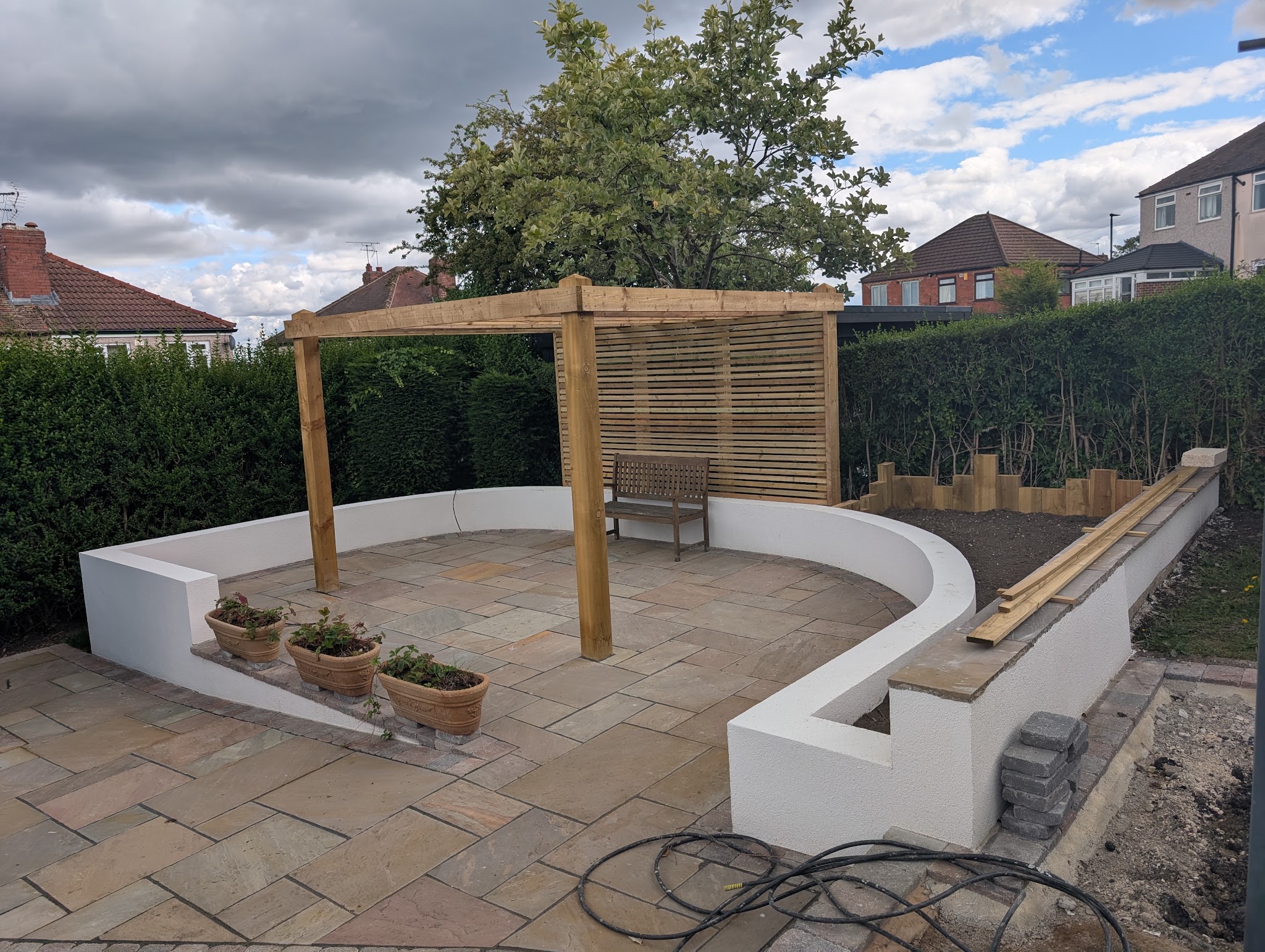 Finished garden with smooth white rendered curved walls, a sandstone patio and a timber pergola